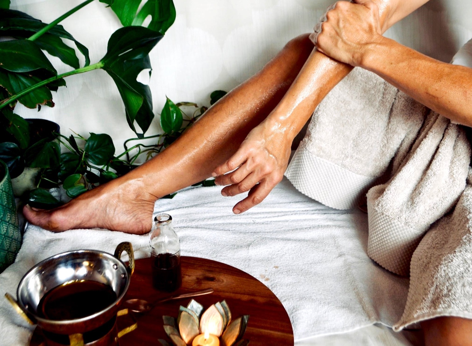 Warm oil self-massage with a bowl of oil, candle and greenery